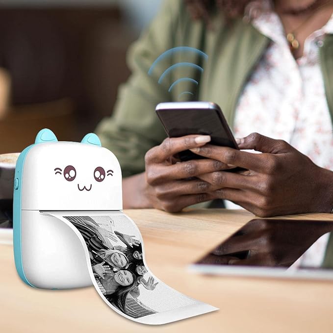 Small printer with cartoon face on a table, printing out an image, with a person using a phone in the background.